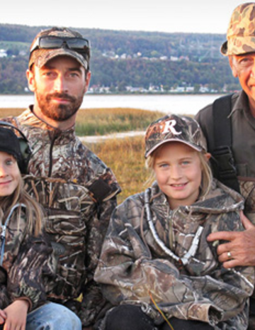 Deux hommes et deux enfants habillées en chasse dans un champs. 