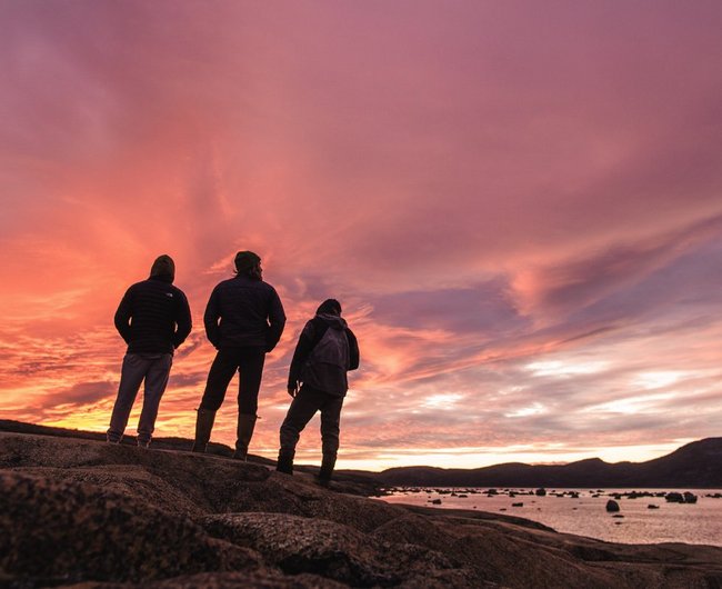 Trois personnes debout sous un couché de soleil rose