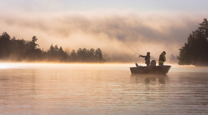 Two fishermen standing in a rowboat in a misty atmosphere