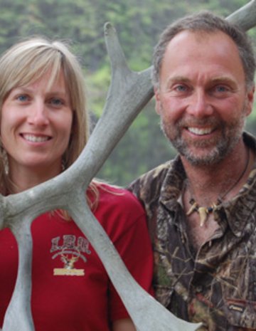 Une femme et un homme chasseurs accotés à un arbre.