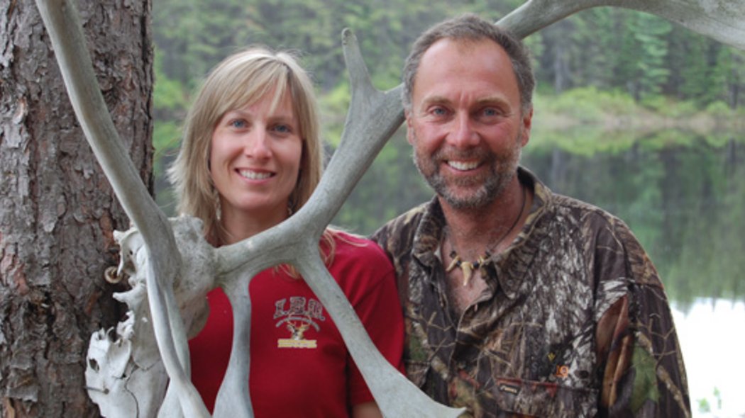 Une femme et un homme chasseurs accotés à un arbre.