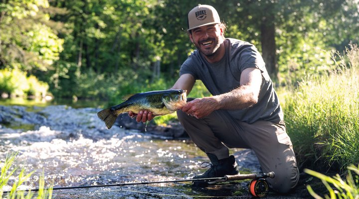 A fisherman in a river with a walleye.