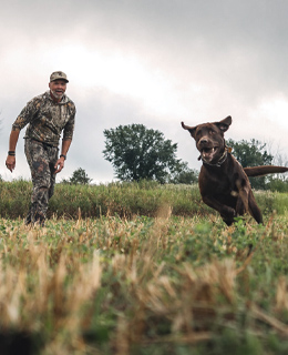 Un chasseur avec son chien qui coure.