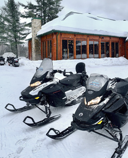 Two snowmobiles in front of an outfitter.