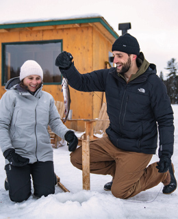 A couple ice fishing on an icy lake.