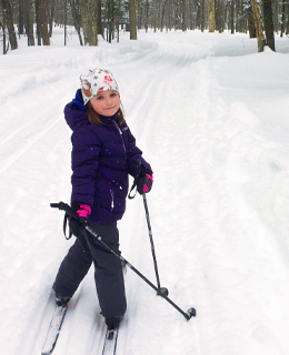 A little girl cross-country skiing on a trail.