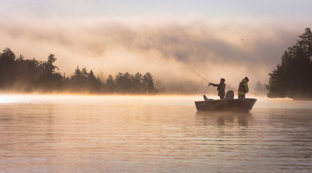 Two fishermen standing in a rowboat in a misty atmosphere