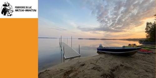 Sunset with a lake view and a boat and Auberge Matchi-Manitou logo