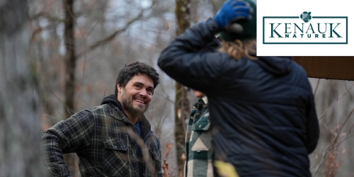 A men in the wood talking with someone else with Kenauk logo